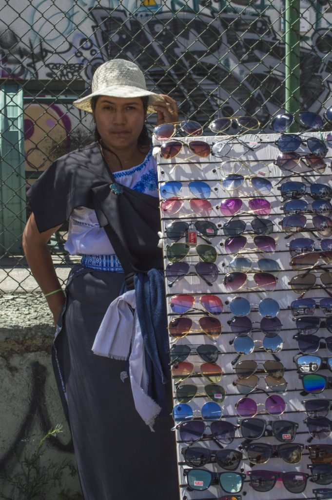 Nelly ofrece gafas y lentes de sol en distintos colores y precios. Protege su rostro con un delgado sombrero plástico. Fotografía: Meche Crespo.